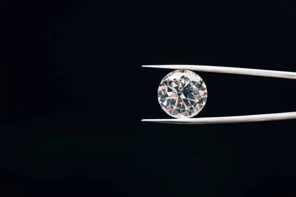 Transparent pure shiny diamond in tweezers isolated on black — Stock Photo