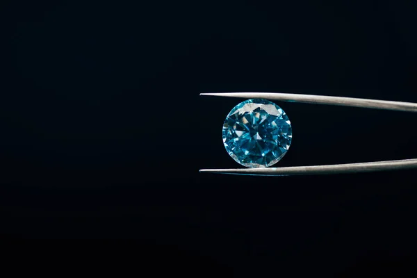 Diamant étincelant bleu coloré dans des pinces isolées sur noir — Photo de stock