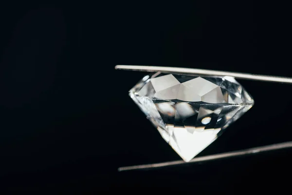 Transparent pure sparkling diamond in tweezers isolated on black — Stock Photo