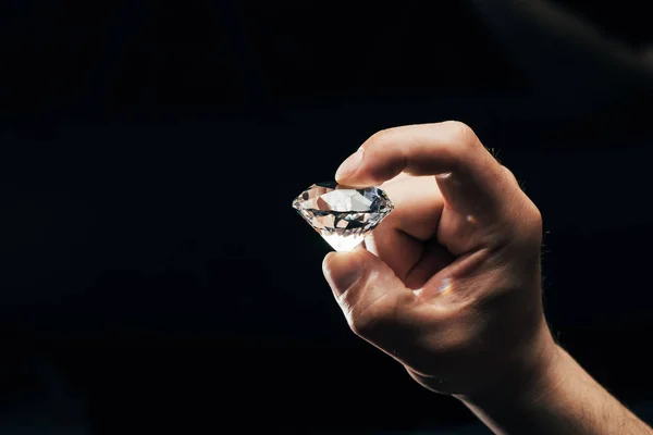 Partial view of man holding big clear shiny diamond isolated on black — Stock Photo