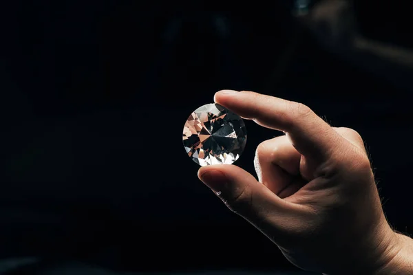 Partial view of man holding big clear shiny diamond on black background — Stock Photo