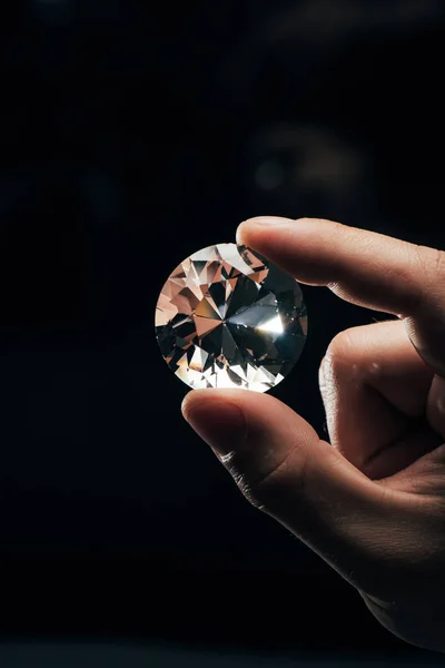 Cropped view of man holding big clear shiny diamond on black background — Stock Photo