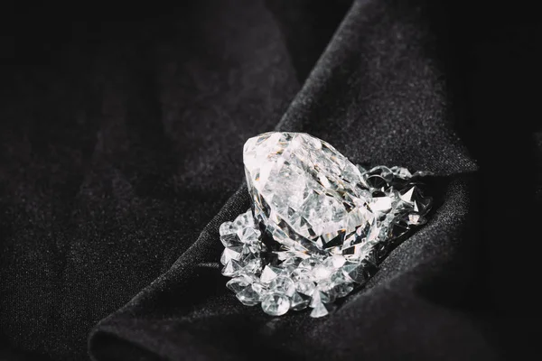 Funkelnder großer Diamant zwischen kleinen auf schwarzem strukturierten glänzenden Tuch — Stockfoto