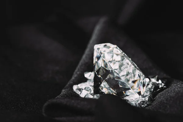 Sparkling pure big diamond among small on black textured shiny cloth — Stock Photo