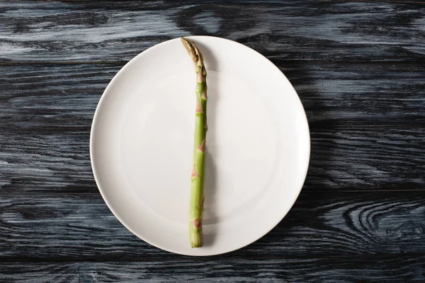 Вид сверху на сырую спаржу на тарелке на сером деревянном фоне — стоковое фото