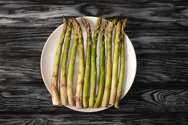 Top view of green organic asparagus on plate on wooden background — Stock Photo