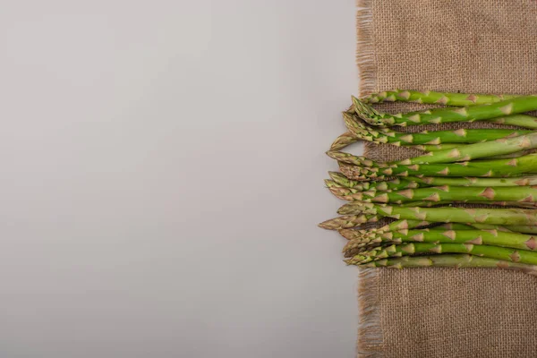 Vista superior de espargos crus verdes em pano de saco em fundo cinza — Fotografia de Stock