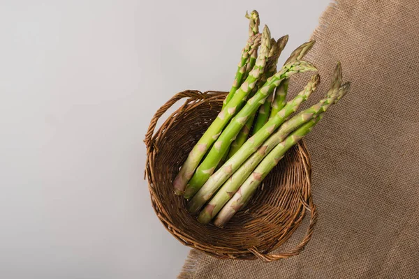 Vue de dessus des asperges vertes dans le panier en osier près du sac sur fond gris — Photo de stock