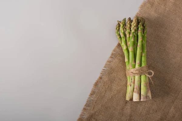 Vista dall'alto di mazzo di asparagi verdi legati con corda vicino al sacco su sfondo grigio — Foto stock