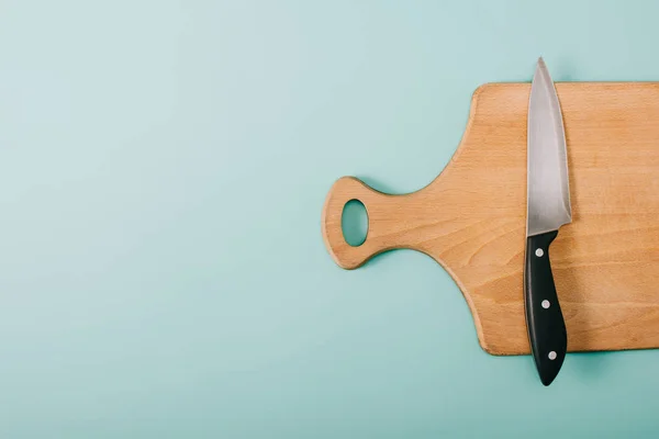 Draufsicht auf Holzschneidebrett mit Messer auf blauem Hintergrund mit Kopierraum — Stockfoto