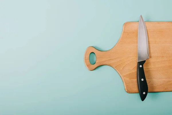 Vista superior de tabla de cortar de madera con cuchillo sobre fondo azul con espacio de copia - foto de stock
