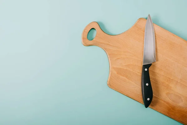 Top view of wooden cutting board with knife on blue background — Stock Photo