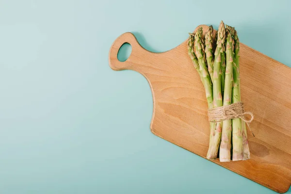 Ansicht von grünem rohen Spargel auf Holzschneidebrett auf blauem Hintergrund — Stockfoto