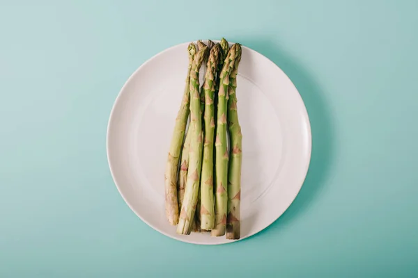 Vista dall'alto di asparagi grezzi verdi su piatto bianco su sfondo blu — Foto stock