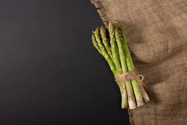 Vue de dessus du bouquet d'asperges vertes attachées avec une corde près du sac sur fond noir — Photo de stock