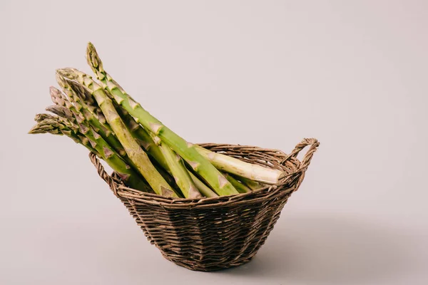 Haufen grünen ungekochten Spargels in Weidenkorb auf grauem Hintergrund — Stockfoto