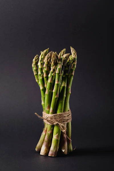 Mazzo di asparagi crudi verdi legati con corda su fondo nero — Foto stock