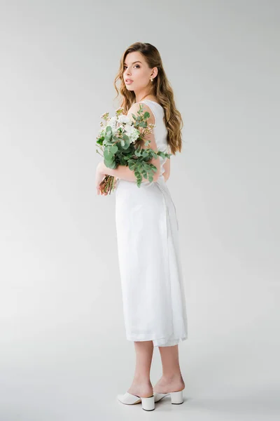 Junge Frau im weißen Kleid hält, während sie auf grau steht — Stockfoto