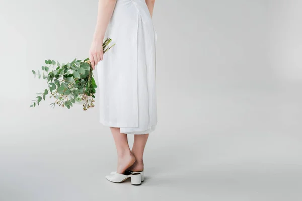 Vista recortada de la chica en vestido sosteniendo flores mientras está de pie en gris - foto de stock