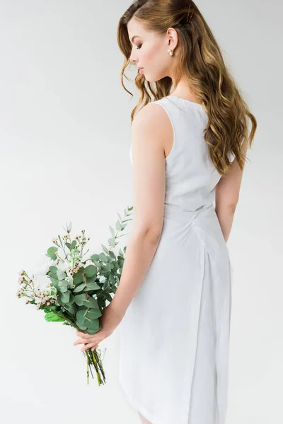 Mujer atractiva en vestido elegante mirando flores en blanco - foto de stock