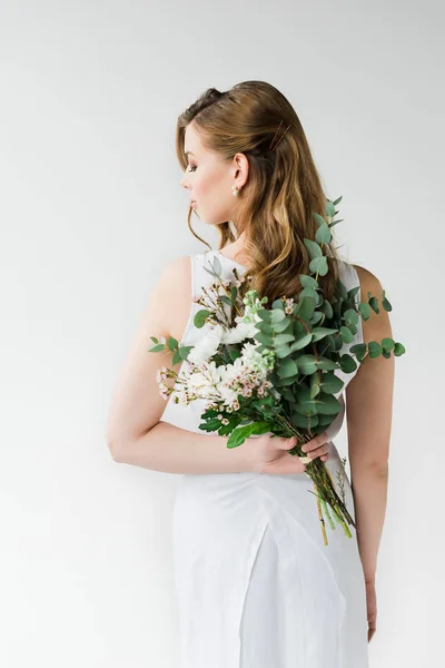 Back view of woman in elegant dress holding flowers behind back on white — Stock Photo