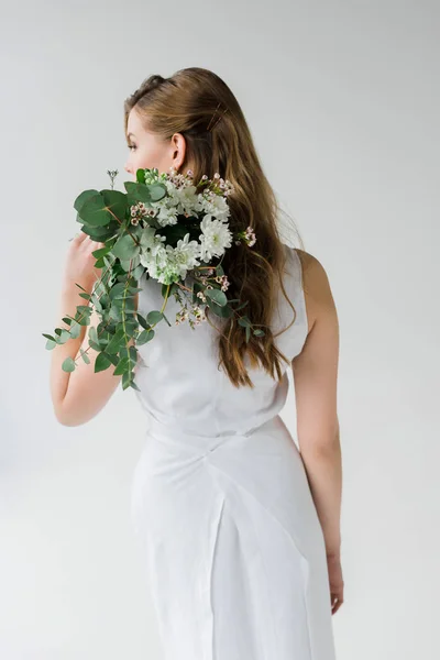 Вид сзади девушки в платье, держащей цветы за спиной, изолированной на белом — стоковое фото