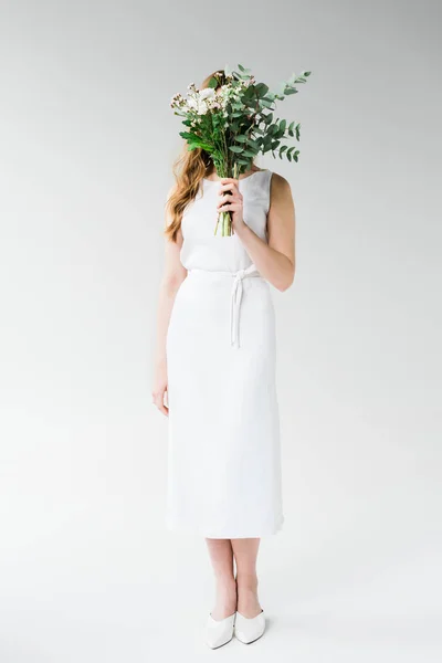 Femme en robe couvrant visage avec des fleurs sur blanc — Photo de stock