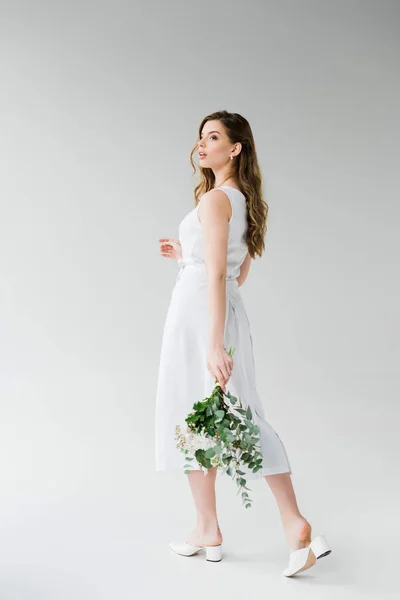 Приваблива дівчина в сукні, що йде з квітами на сірому — стокове фото