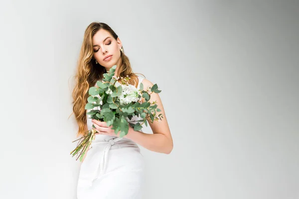 Elegante ragazza in vestito che tiene bouquet di fiori di camelacio e crisantemo con foglie di eucalipto su bianco — Foto stock