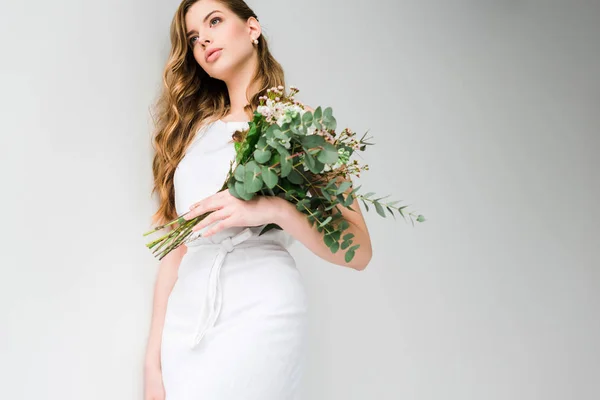Low angle view of girl in dress holding bouquet of chamelacium and chrysanthemum flowers with eucalyptus leaves on white — Stock Photo