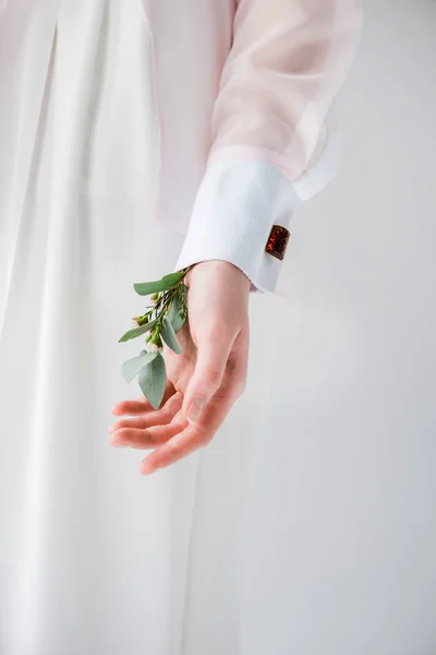 Vue recadrée de la jeune femme debout avec des feuilles d'eucalyptus et des fleurs à la main sur gris — Photo de stock