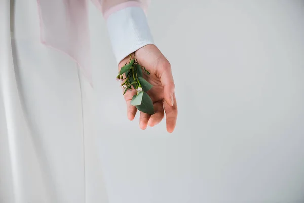 Vista ritagliata di ragazza in piedi con foglie di eucalipto e fiori in mano sul grigio — Foto stock
