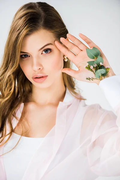 Красива дівчина з квітами і зеленим листям евкаліпта в руці дивиться на камеру на білому — стокове фото