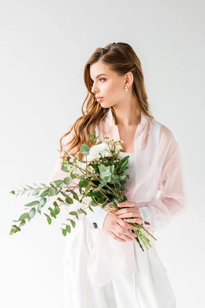 Atractiva chica sosteniendo flores y hojas de eucalipto verde sobre blanco - foto de stock
