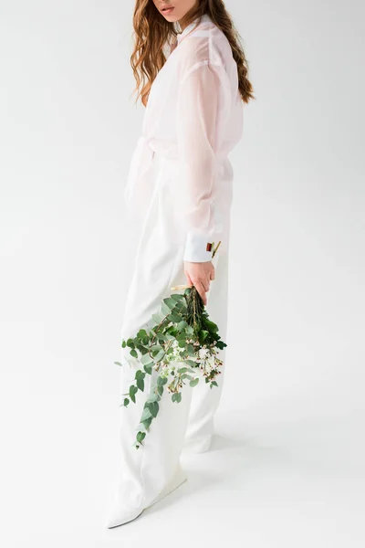 Vista recortada de la mujer sosteniendo hojas de eucalipto verde con flores en blanco - foto de stock