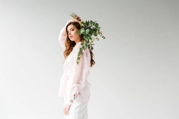 Hermosa mujer joven sosteniendo flores con hojas de eucalipto verde detrás de nuevo en blanco - foto de stock