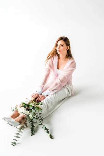 Jovem mulher elegante sentado com flores e eucalipto verde no branco — Fotografia de Stock