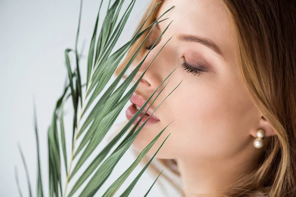 Attraente ragazza con gli occhi chiusi vicino foglia di palma verde su bianco — Foto stock