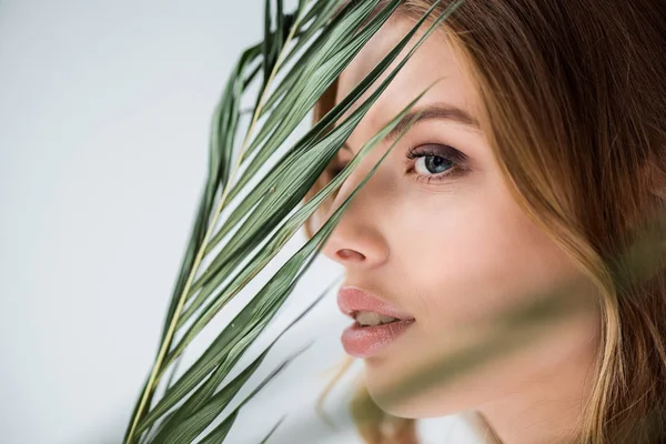 Beautiful young woman near green palm leaf on white — Stock Photo
