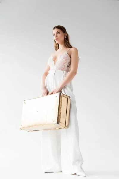 Низкий угол зрения на красивую девушку, держащую чемодан, стоя на белом — стоковое фото