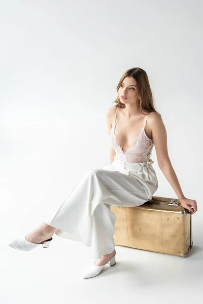 Rêveuse belle jeune femme assise sur un sac de voyage sur blanc — Photo de stock