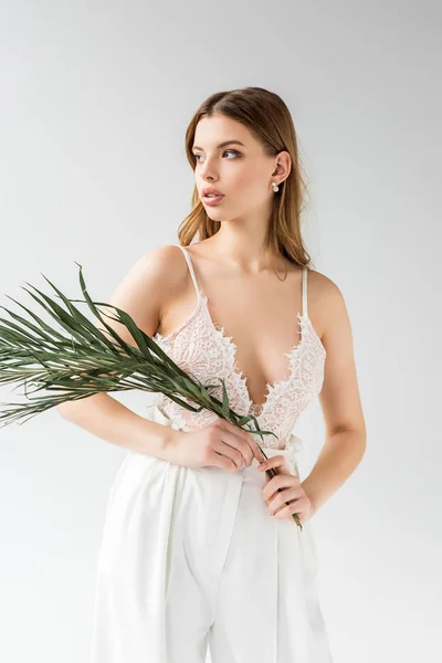 Elegante ragazza che tiene foglia di palma verde mentre in piedi su bianco — Foto stock