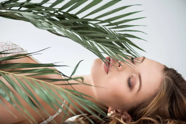 Attraktive junge Frau liegt in der Nähe tropischer Palmenblätter mit geschlossenen Augen auf weißem Grund — Stockfoto