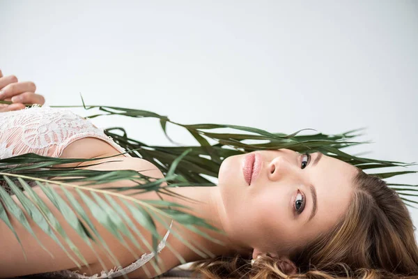 Hermosa joven tumbada cerca de hojas de palmeras tropicales en blanco - foto de stock