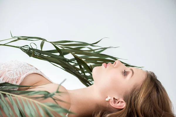 Side view of attractive young woman lying near tropical palm leaves on white — Stock Photo
