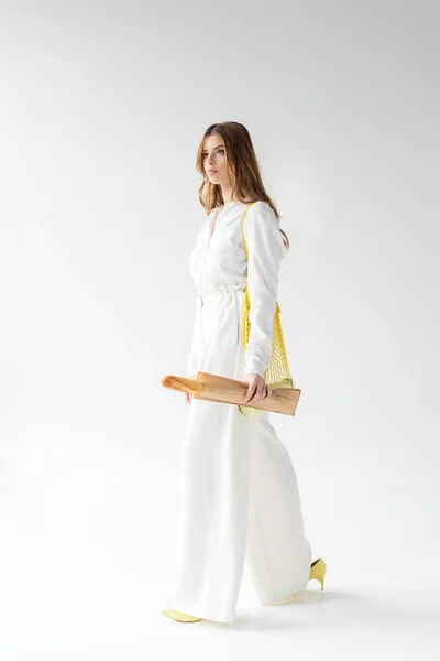 Jolie femme marchant avec baguette dans un sac en papier et sac à ficelle jaune sur blanc — Photo de stock