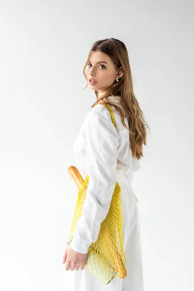 Atractiva mujer con baguette y botella de leche en bolsa de hilo amarillo sobre blanco - foto de stock