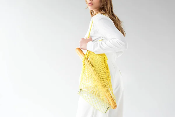 Cropped view of woman with baguette and bottle of milk in yellow string bag on white — Stock Photo