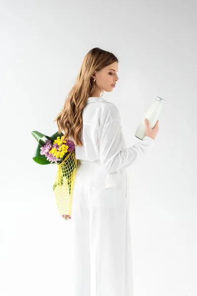 Mulher atraente segurando garrafa de leite e saco de corda amarela com flores silvestres no branco — Fotografia de Stock