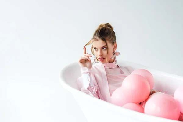 Attractive girl lying in bathtub with pink air balloons on white — Stock Photo